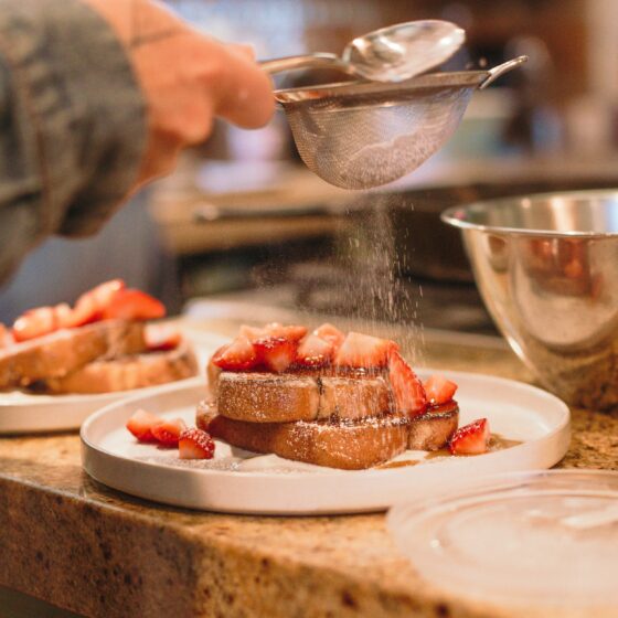 French toast with strawberries being sprinkled with powdered sugar